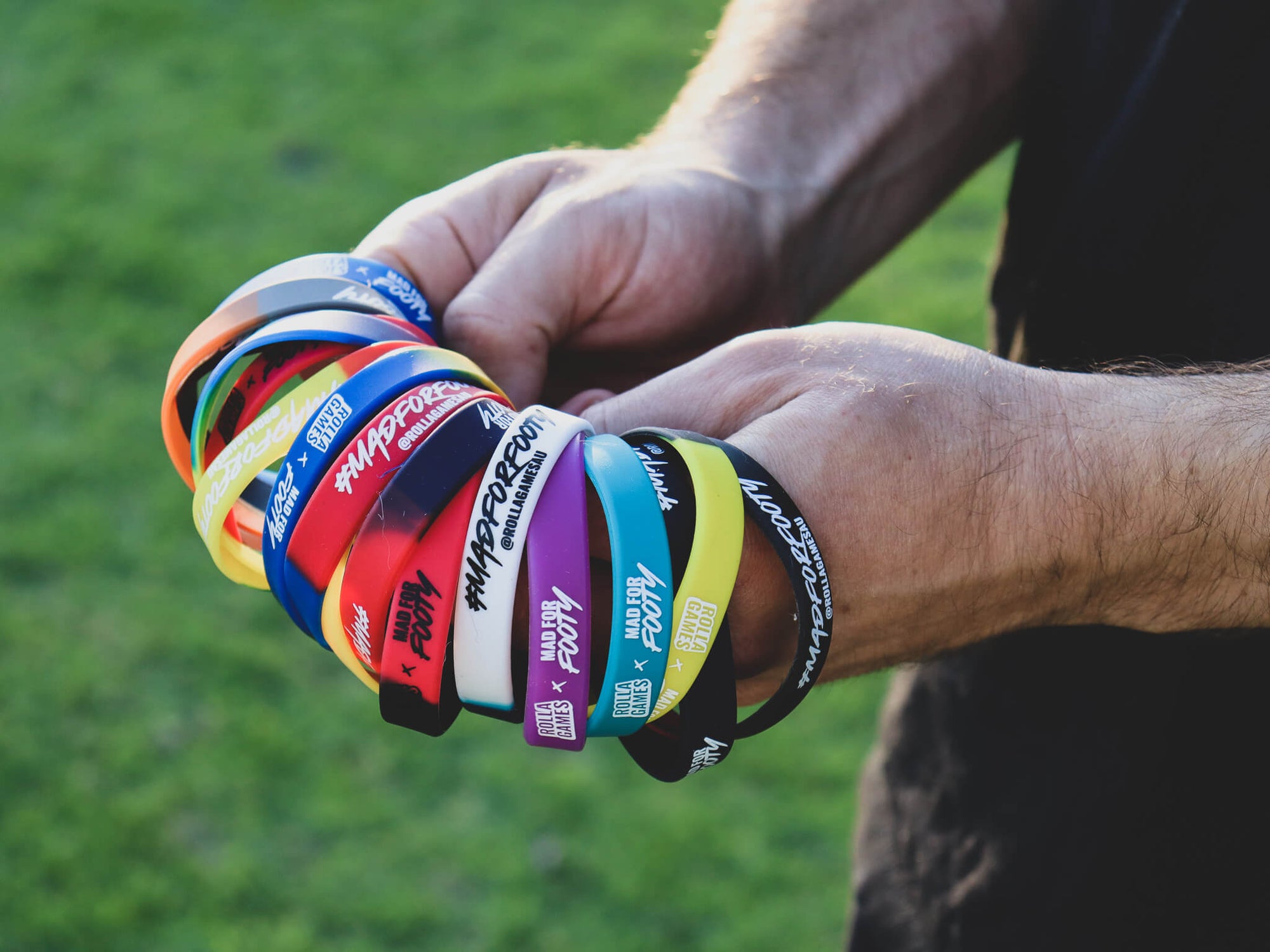 Holding a handful of colourful AFL football club wristbands.