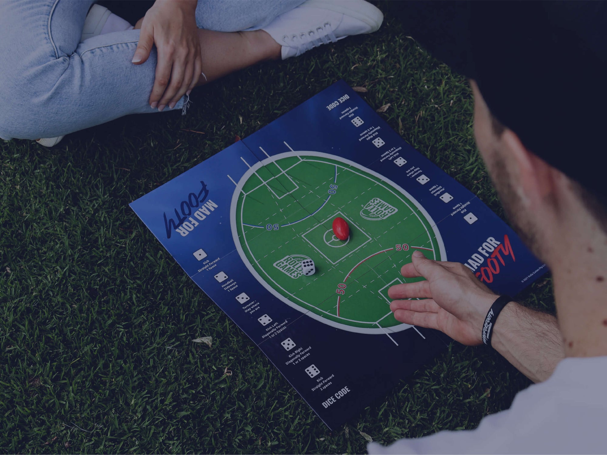 Rolling a dice and playing the Australian Rules Football Board Game on the grass.
