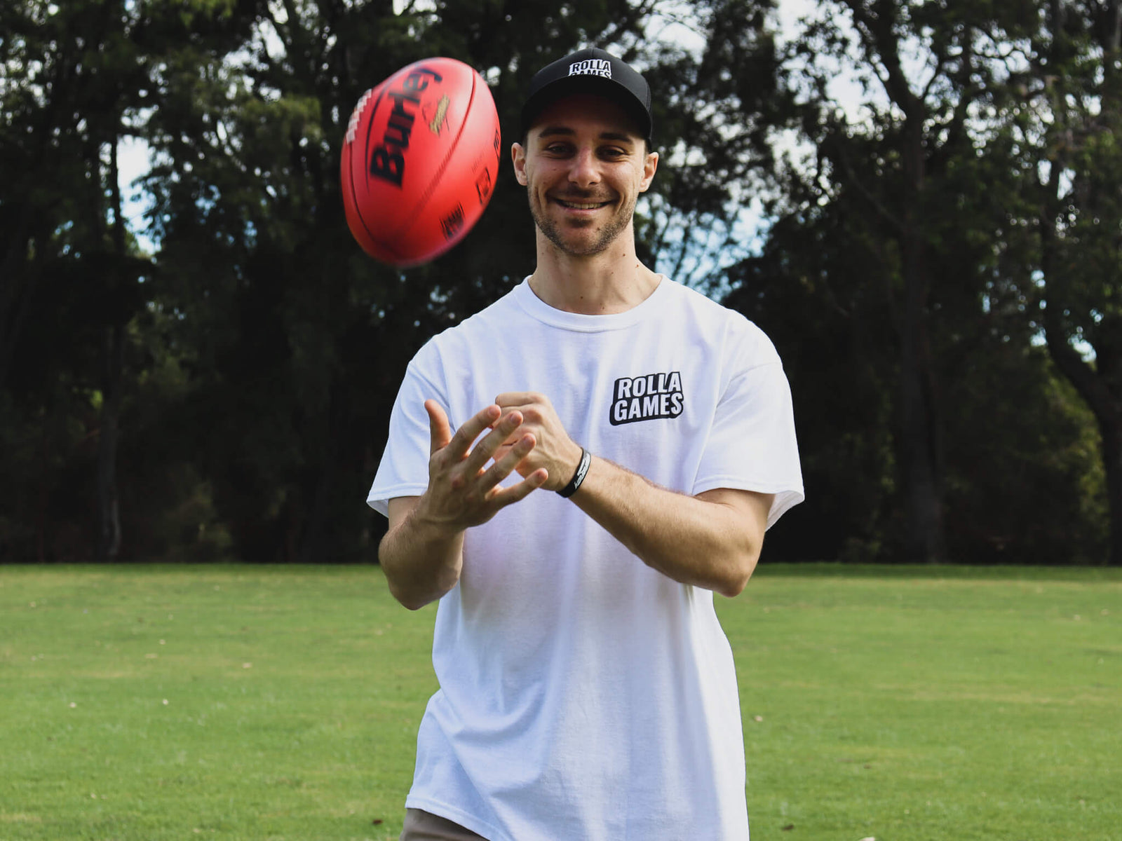 Male wearing black hat handballing an AFL football.