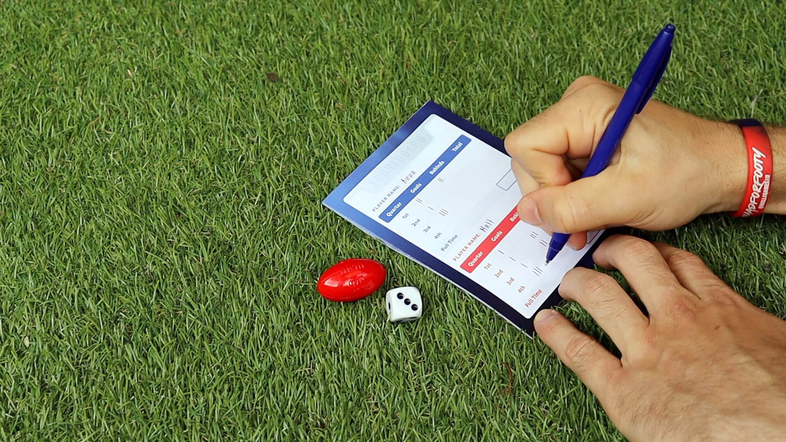 Writing football score on scorecard on grass next to dice and red afl moulded counter.