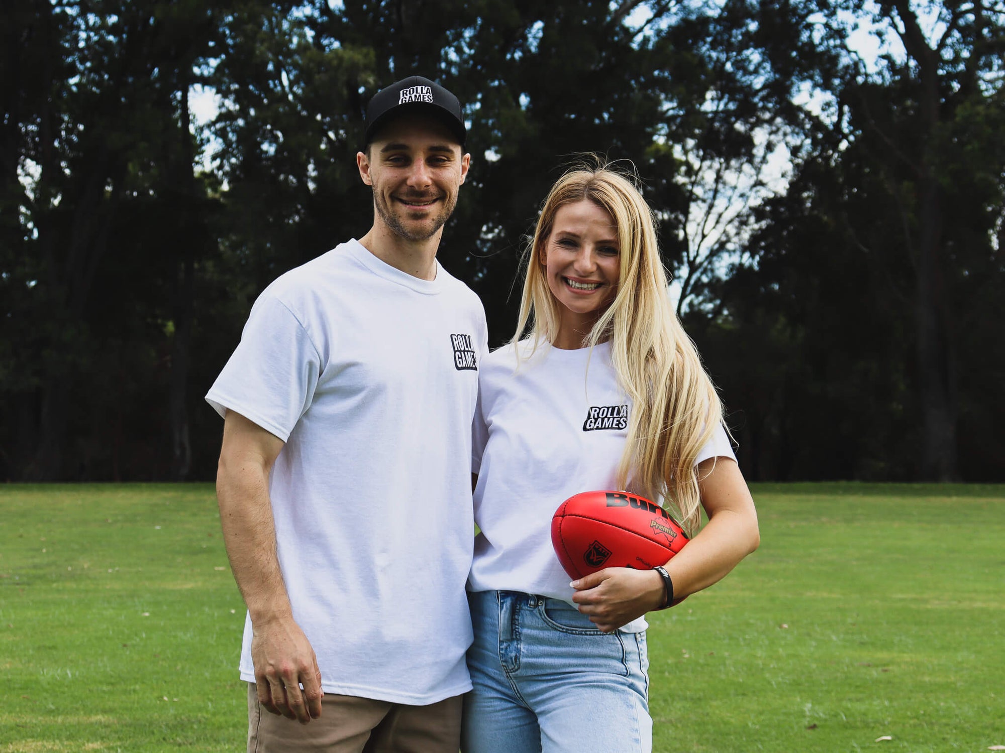Male and female smiling, casually holding an AFL football.